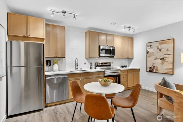 a kitchen with stainless steel appliances granite countertop a refrigerator a stove a sink a dining table and chairs with wooden floor