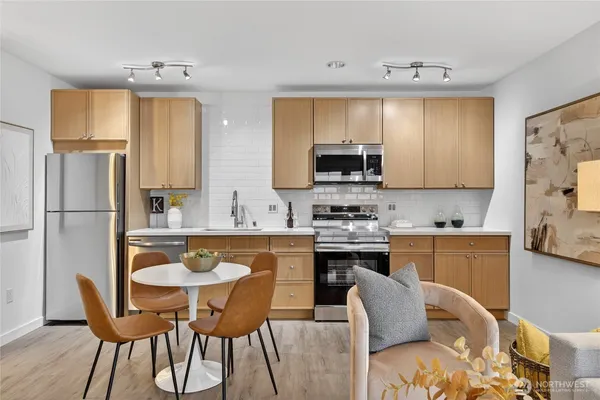 a kitchen with stainless steel appliances a stove a sink dishwasher a refrigerator with a dining table and chairs