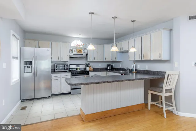 a kitchen with stainless steel appliances granite countertop a refrigerator a sink dishwasher a stove and white cabinets with wooden floor