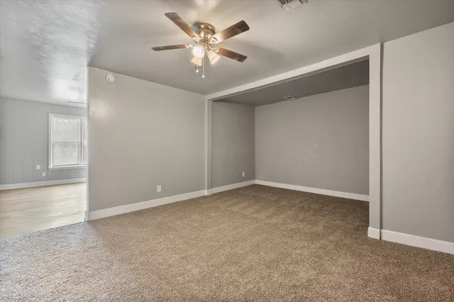 an empty room with a chandelier fan and windows