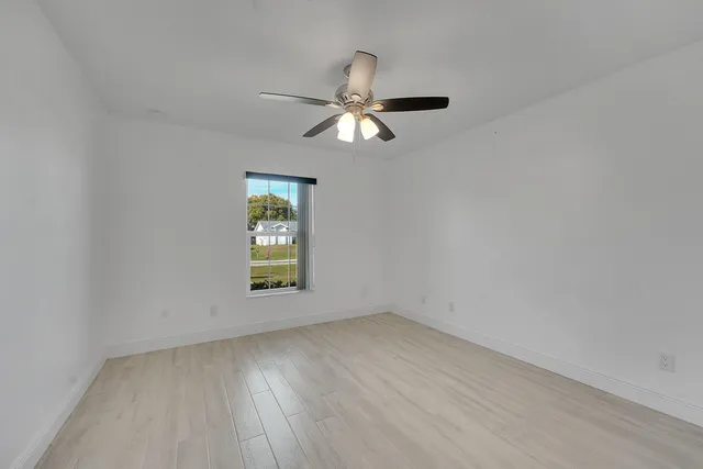 an empty room with wooden floor chandelier fan and windows