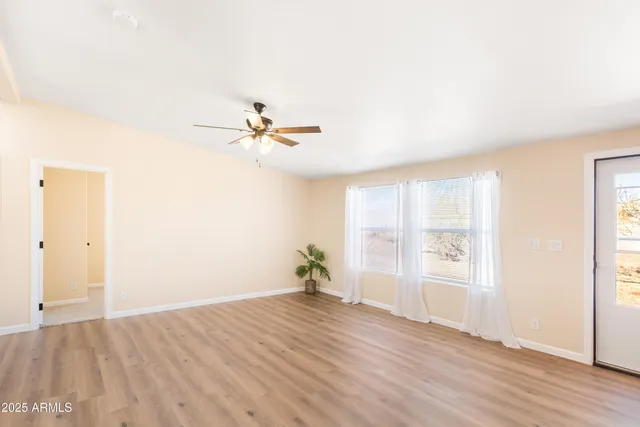 an empty room with wooden floor chandelier fan and windows