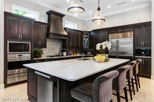595 Regatta Road Naples, FL 34103 - Photo 12 of 40 Gourmet kitchen featuring dark wood cabinetry, stainless steel appliances, a large center island with a white countertop, and tiled flooring