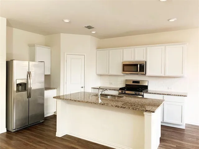 a kitchen with stainless steel appliances granite countertop a refrigerator a stove a sink and white cabinets with wooden floor