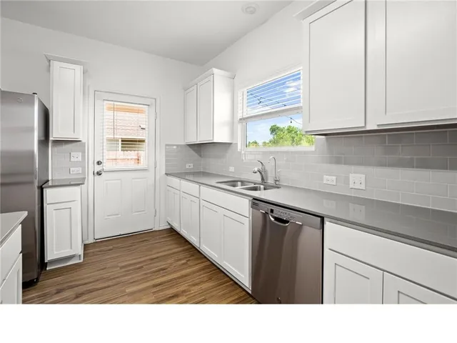 a kitchen with stainless steel appliances granite countertop a sink dishwasher a refrigerator and cabinets with wooden floor