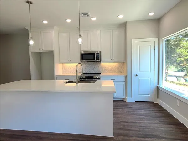 a large kitchen with stainless steel appliances a large counter top a stove a kitchen island a refrigerator and a view of living room