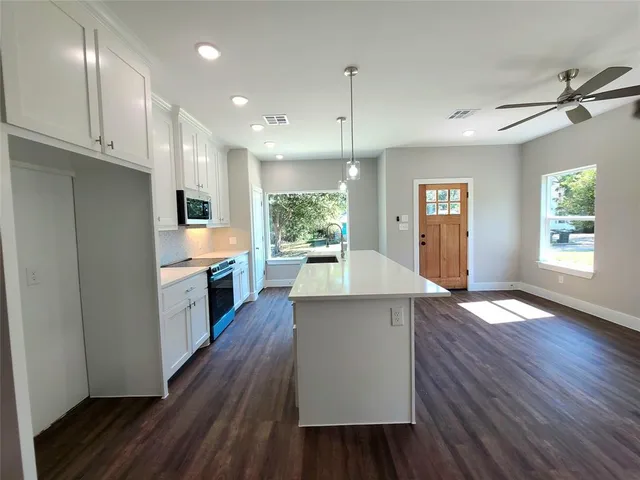 a kitchen with stainless steel appliances granite countertop a refrigerator a sink dishwasher a stove and white countertops with wooden floor