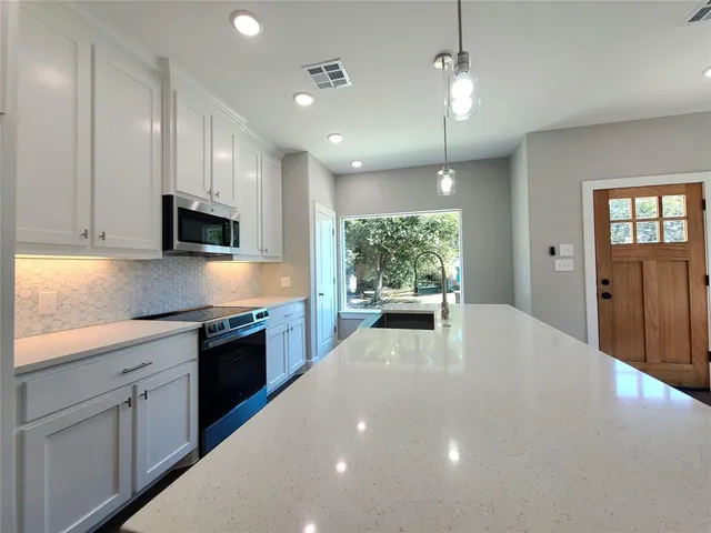 a large white kitchen with stainless steel appliances granite countertop a stove a sink a refrigerator white cabinets and wooden floor