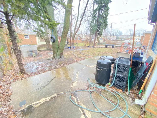 a view of a backyard with table and chairs and a barbeque with potted plants and large trees