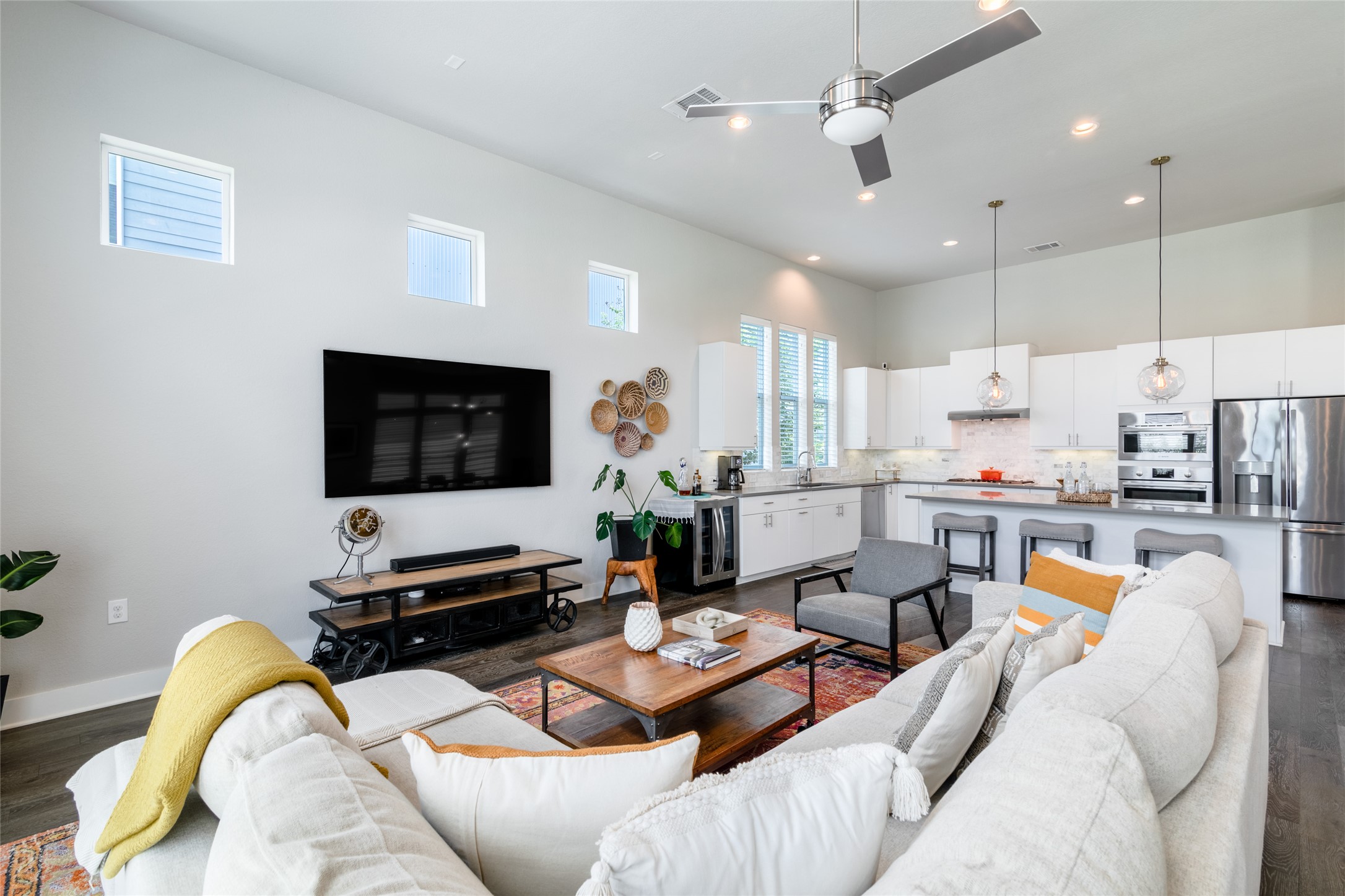 6025 Seville Drive Austin, TX 78724 - Photo 10 of 40 Open-concept living space featuring high ceilings, wood-finish flooring, view of modern kitchen with stainless steel appliances, a kitchen island with seating, and recessed lighting