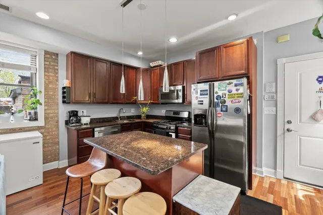 a kitchen with stainless steel appliances granite countertop a refrigerator a stove a sink a dining table and chairs with wooden floor