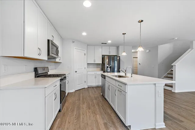 a kitchen with a stove a sink a refrigerator and white cabinets with wooden floor