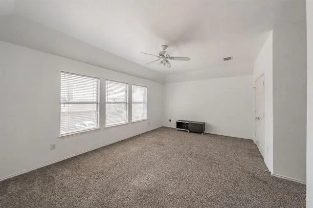 an empty room with chandelier fan and windows