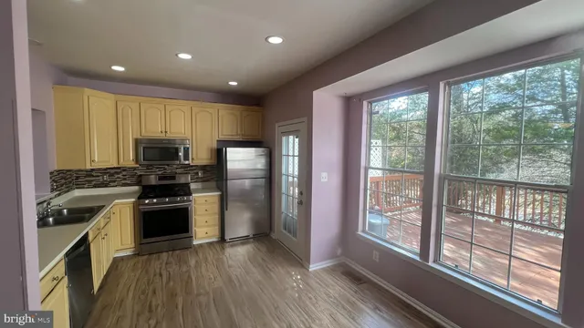 a kitchen with stainless steel appliances granite countertop a refrigerator oven a sink with wooden cabinets and wooden floor