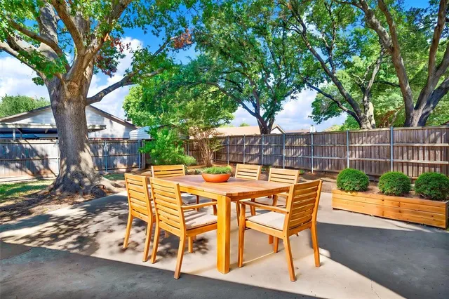 a view of a patio with table and chairs with wooden fence and large trees