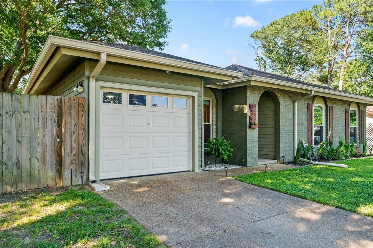 Front exterior featuring a single-car garage with transom windows, a brick facade, arched entryway, and landscaped front yard