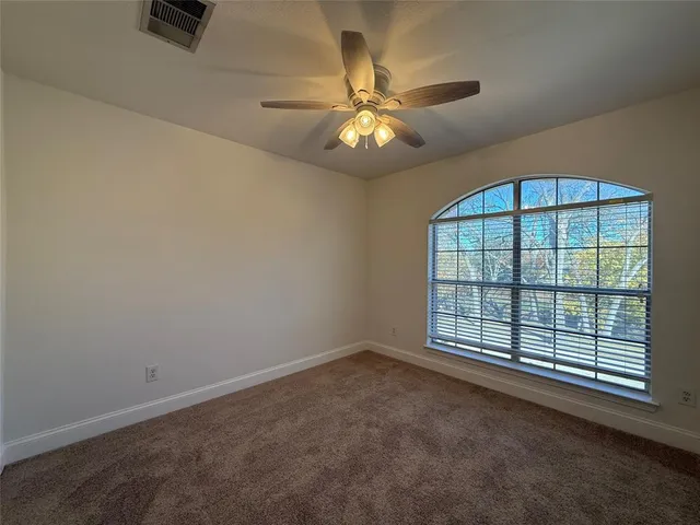 an empty room with chandelier fan and windows