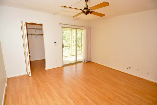 an empty room with wooden floor fan and windows