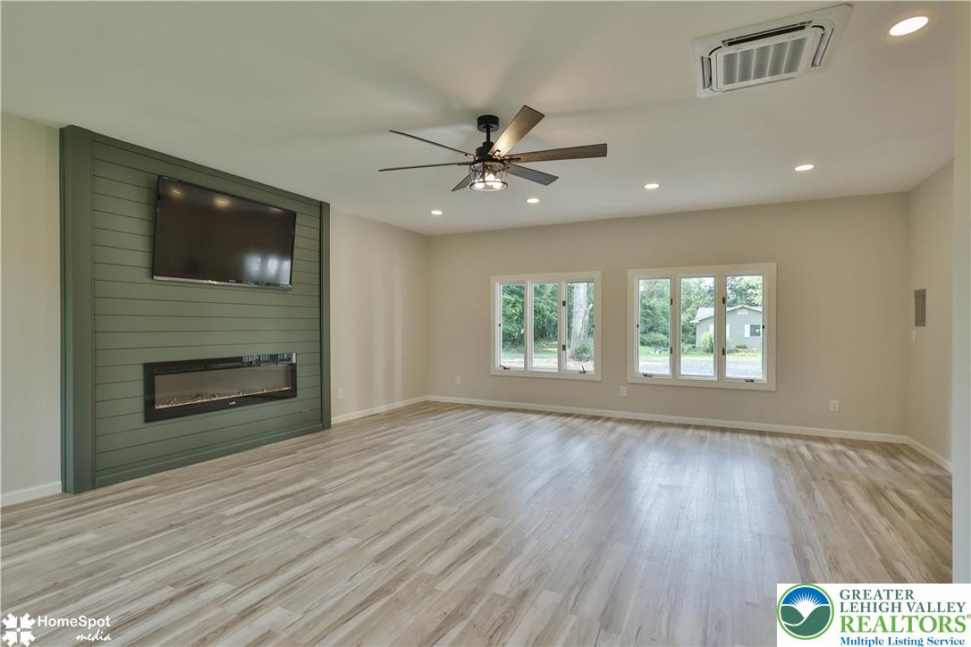 919 Point Phillips Road Bath, PA 18014 - Photo 23 of 59 A spacious living area features a modern shiplap accent wall with an electric fireplace, light wood-look flooring, and ample natural illumination through large windows.