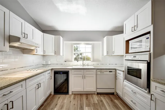 a kitchen with granite countertop white cabinets sink and stainless steel appliances