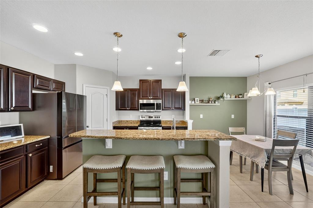 11214 Carrick Stone Street Wimauma, FL 33598 - Photo 19 of 73 a kitchen with stainless steel appliances kitchen island granite countertop a table chairs microwave and sink