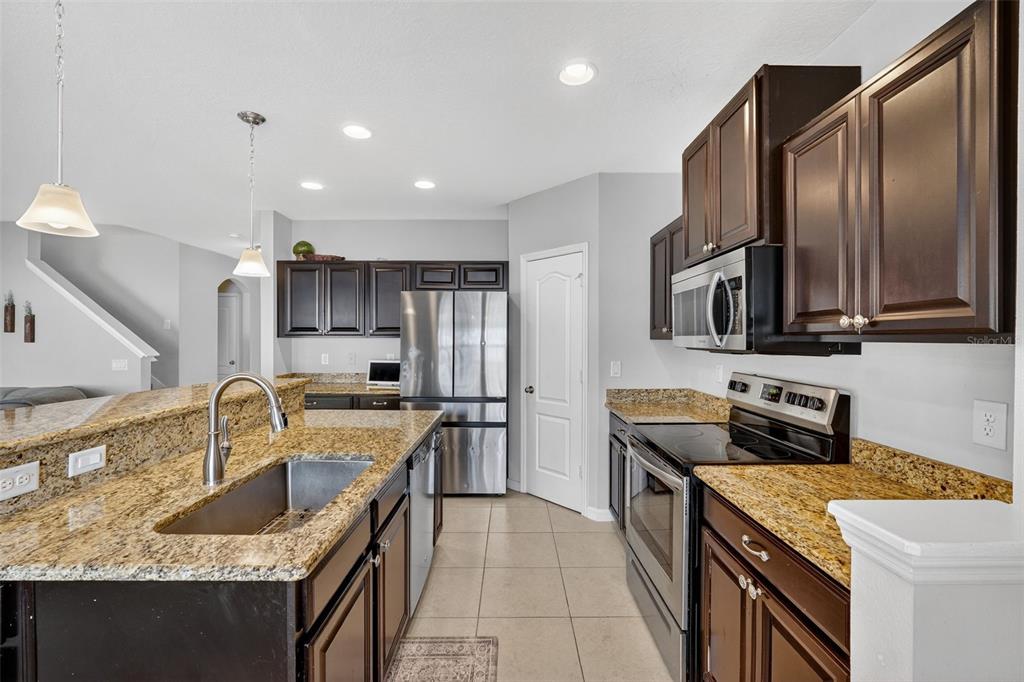 11214 Carrick Stone Street Wimauma, FL 33598 - Photo 25 of 73 a kitchen with stainless steel appliances granite countertop a sink a stove and a refrigerator