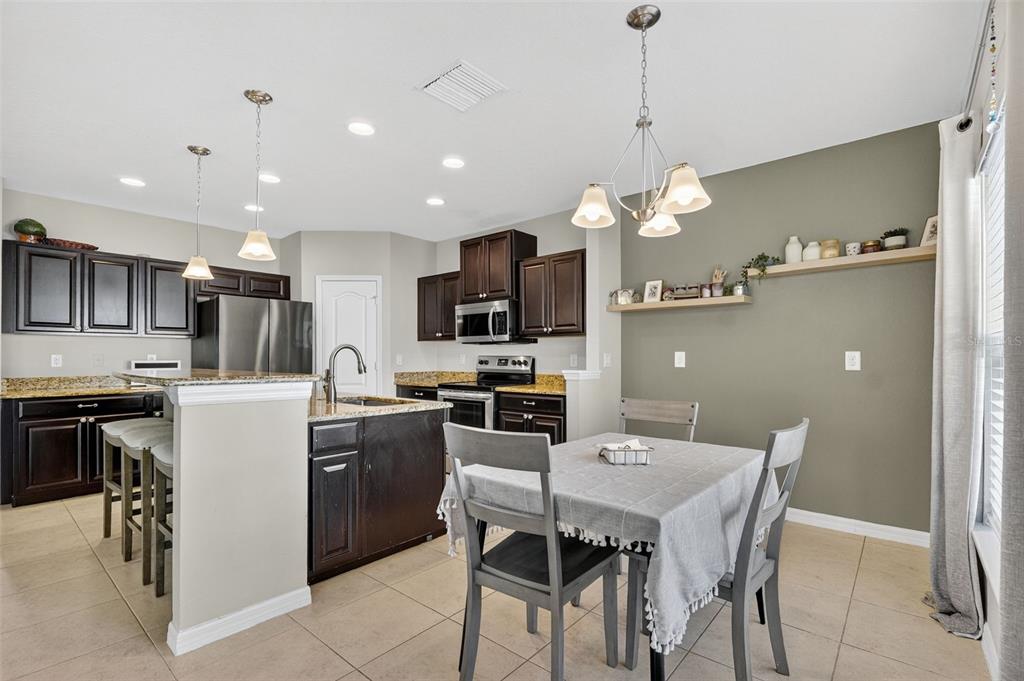 11214 Carrick Stone Street Wimauma, FL 33598 - Photo 26 of 73 a kitchen with a refrigerator a stove a sink a dining table and chairs