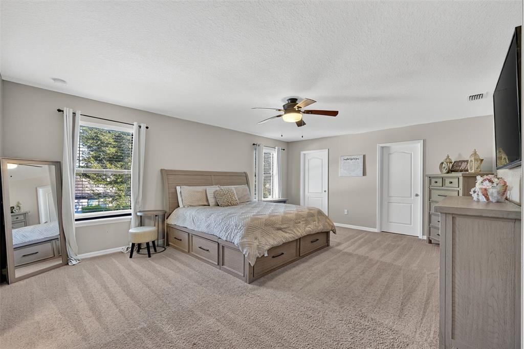 11214 Carrick Stone Street Wimauma, FL 33598 - Photo 34 of 73 a spacious bedroom with a bed and a chandelier