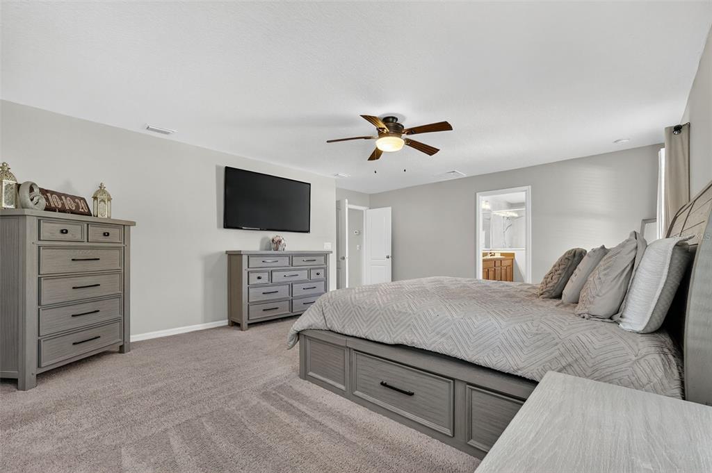 11214 Carrick Stone Street Wimauma, FL 33598 - Photo 38 of 73 a spacious bedroom with a bed a dresser and a flat screen tv