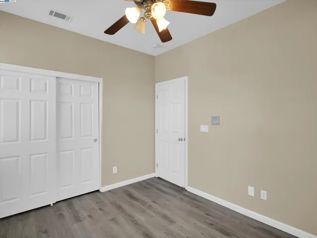 an empty room with wooden floor closet ceiling fan and windows