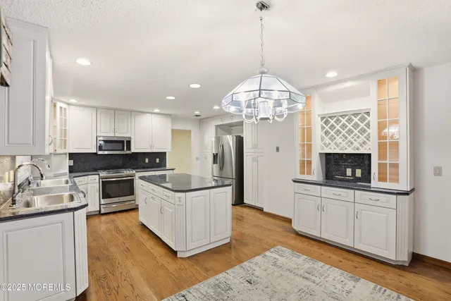 a kitchen with stainless steel appliances granite countertop a refrigerator a sink dishwasher a stove and white cabinets with wooden floor