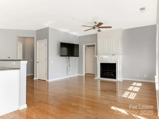 a view of a livingroom with a fireplace a ceiling fan and a kitchen space