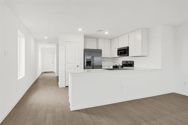 a view of kitchen with stainless steel appliances granite countertop a stove a sink a refrigerator and white cabinets with wooden floor