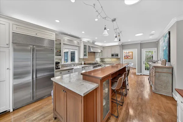 a kitchen with stainless steel appliances granite countertop a kitchen island a stove a refrigerator a sink a dining table and chairs with wooden floor