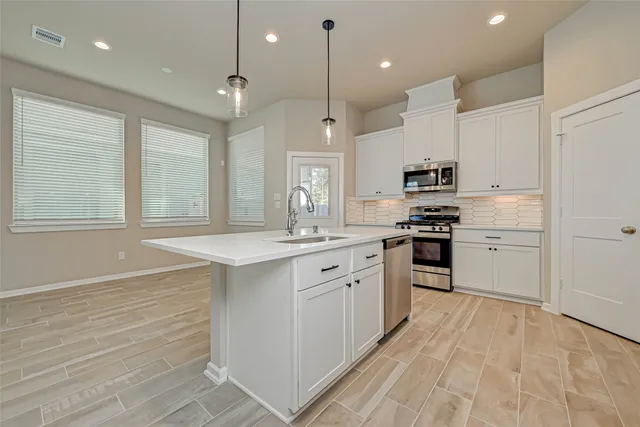 a large kitchen with granite countertop a stove a sink a refrigerator and white cabinets with wooden floor