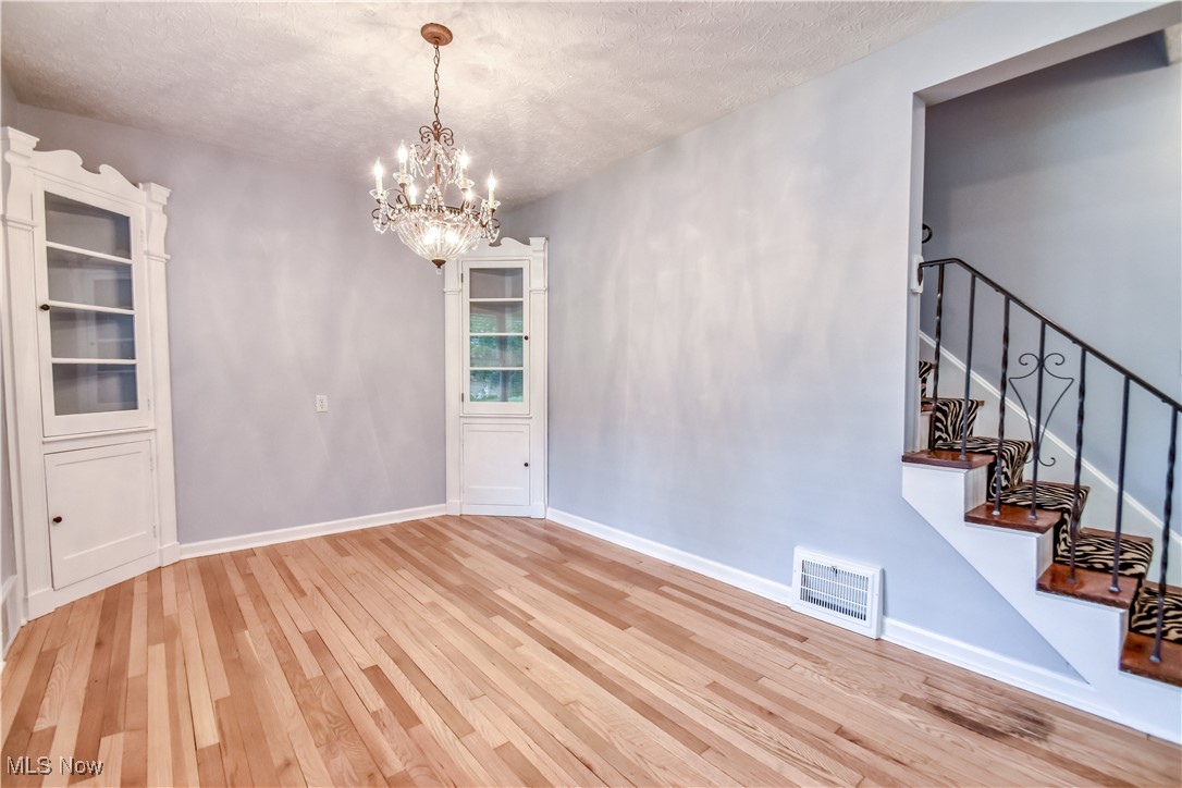8115 Stockbridge Road Mentor, OH 44060 - Photo 9 of 46 Unfurnished dining area with light wood finished floors, a chandelier, a textured ceiling, and stairway