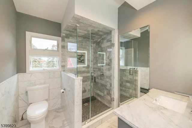 a bathroom with a granite countertop sink a toilet a large mirror and shower