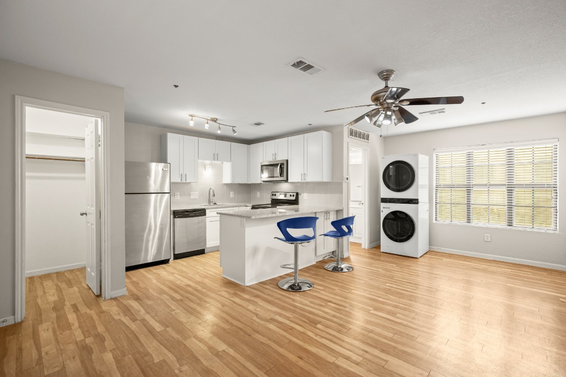 Kitchen featuring appliances with stainless steel finishes, white cabinets, a breakfast bar area, stacked washer / drying machine, and light wood-style flooring