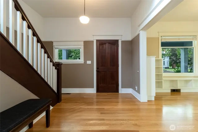 a view of a hallway to an empty room with wooden floor and windows