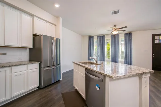 a kitchen with stainless steel appliances granite countertop a refrigerator a sink a stove and white cabinets with wooden floor