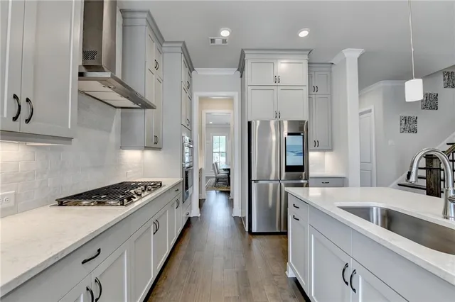 a kitchen with stainless steel appliances granite countertop a stove a sink dishwasher a refrigerator and white cabinets with wooden floor