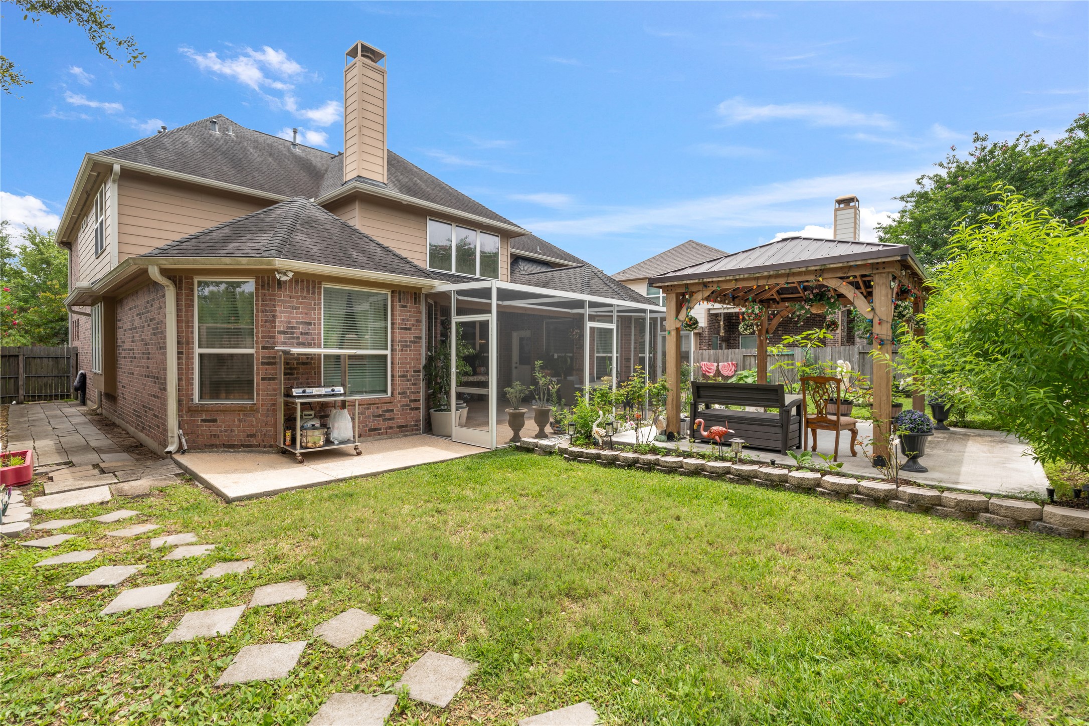 5802 Layton Meadows Lane Spring, TX 77379 - Photo 40 of 42 Full backyard overview. Shows the entire layout — screened-in patio attached to the brick home, the wood gazebo with string lights, stepping stone path, and manicured lawn. Best wide shot of the yard.