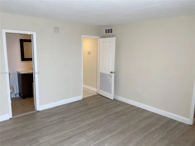 a view of an empty room with wooden floor & cabinet and a window