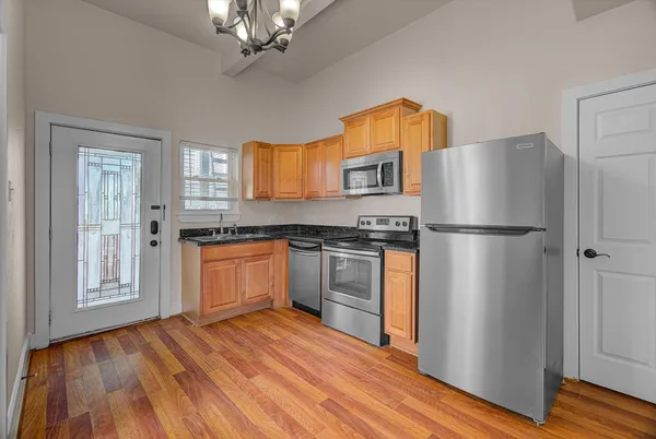 a kitchen with granite countertop a refrigerator a sink dishwasher a stove and white cabinets with wooden floor