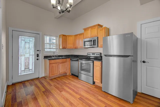 a kitchen with granite countertop a refrigerator a sink dishwasher a stove and white cabinets with wooden floor