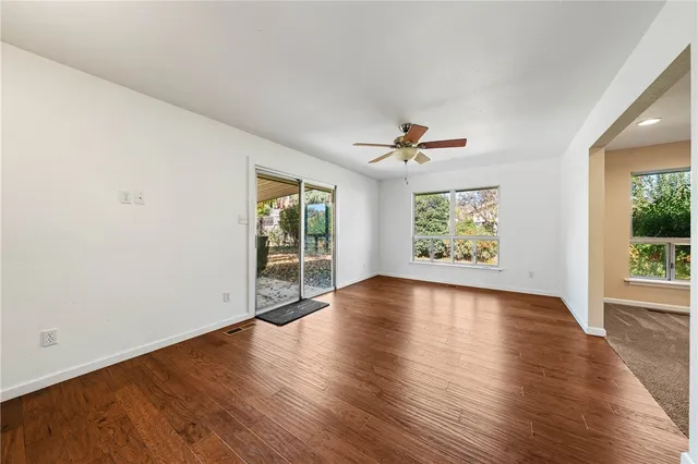 an empty room with wooden floor kitchen view and a window