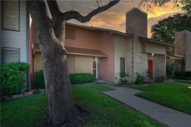 a brick house with a yard plants and a large tree