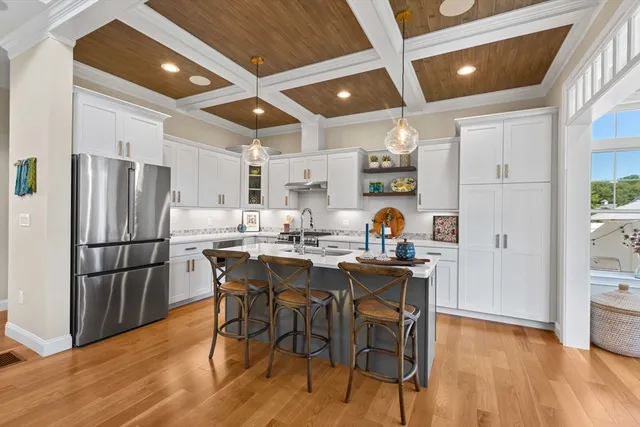 a kitchen with stainless steel appliances a refrigerator a sink dishwasher a dining table and chairs with wooden floor