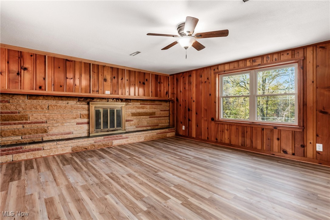 724 Garden Road Zanesville, OH 43701 - Photo 15 of 22 Unfurnished living room featuring light wood-style floors, wooden walls, ceiling fan, and a fireplace