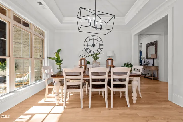 a dining room with wooden floor a chandelier a glass table and chairs